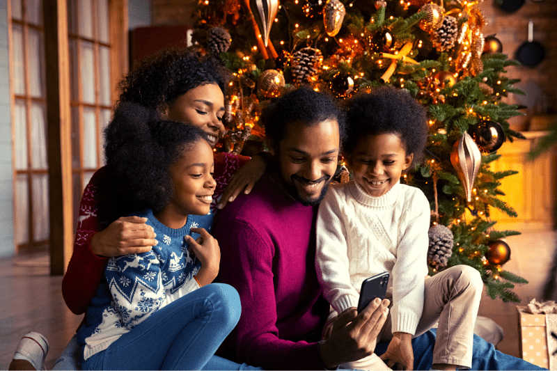 Family looking at smart phone next to Christmas tree